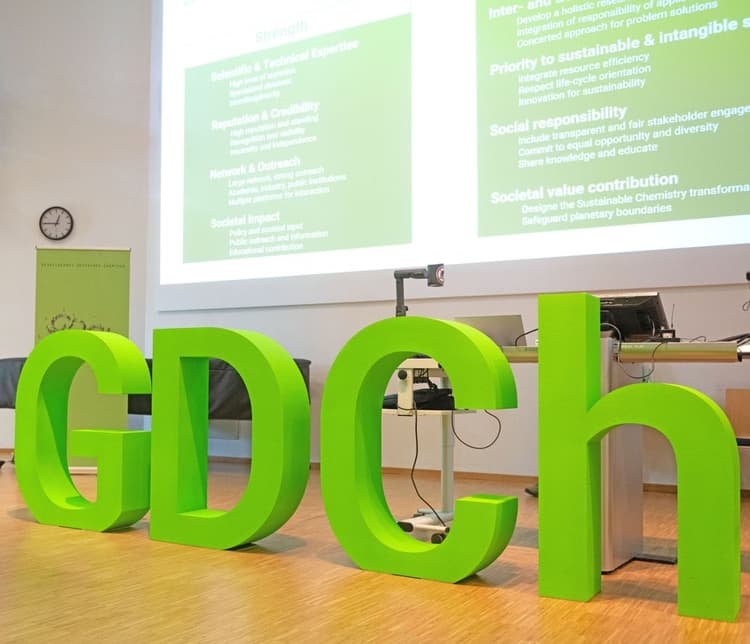 Buchstaben "GDCh" auf einer Bühne. Im Hintergrund Präsentation eines wiss. Vortrags